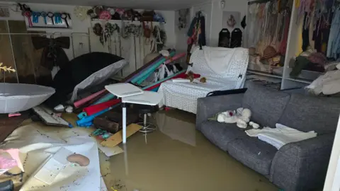 Aga Tetera Photography An image of a flooded room with a sofa and chair covered in a polka dot fabric with materials and unidentifiable equipment engulfed in water