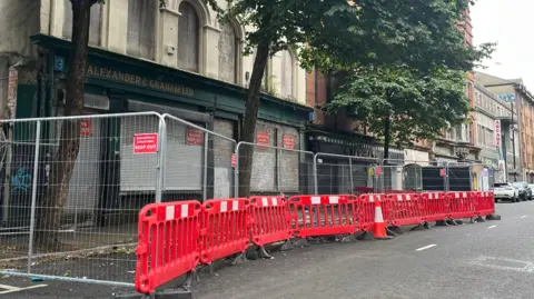 A red safety barrier set up along a road outside a derelict building. 