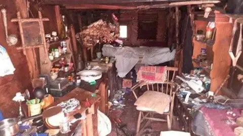 CPS A police photo shows a disgusting interior of a caravan. Rubbish covered every table top and a wooden chair in the middle of the scene 