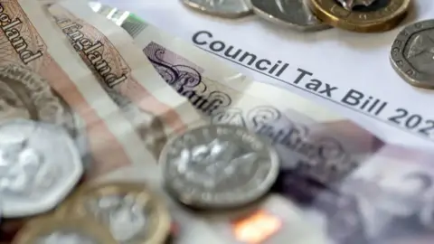 PA Media Image shows bank notes and coins on top of a council tax bill