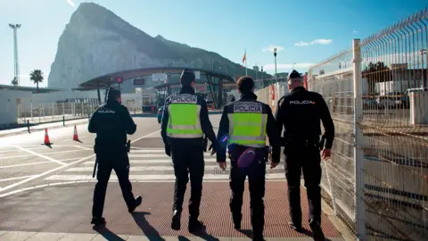 Four Spanish police seen from behind with Spanish Policia bibs at the border of Gibraltar and Spain with thr Rock of Gibraltar in the background