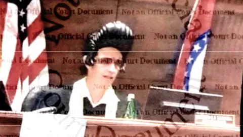 The State of Missouri's Commission on Retirement, Removal and Discipline of Judges An image of Judge Thornhill sitting at the court bench, taken from official court documents, showing him wearing an Elvis wig with the singer's signature black pompadour and sunglasses, as well as a traditional judge's robe with a white scarf around his neck. In front of him is a computer screen and a bottle of water. Behind him is a flag of the US and a flag of the State of Missouri. 