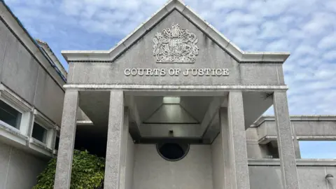 Outside the front of Truro Crown Court in Cornwall. It is a grey stone building with the words "courts of justice" written on the wall.