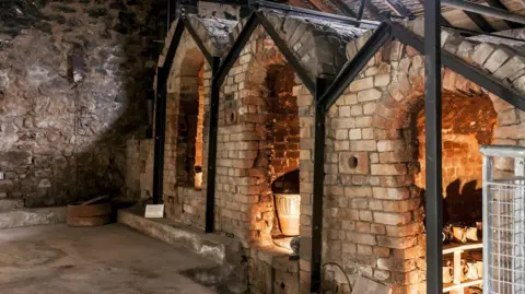 Matthew Tyas The climbing kilns at Leach Pottery look like sheds made of bricks with open doorways. Inside them are shelves with pots ready for firing.
