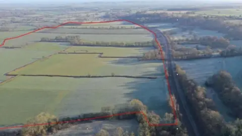 A drone shot of fields and countryside, a large red line drawn round the fields where solar panels would be 