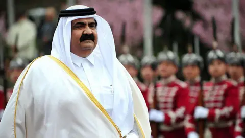 Hamad is seen wearing a white robe as uniformed military guards stand to attention behind him.