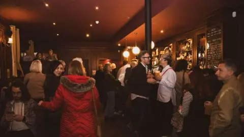 People laughing, talking and drinking in a dimly-lit bar in Sunniside during Sunniside Nights in 2025.