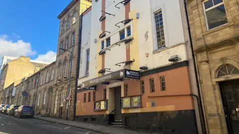 The exterior of the Bradford Playhouse, a cream and orange brick building, with the shutters down. 