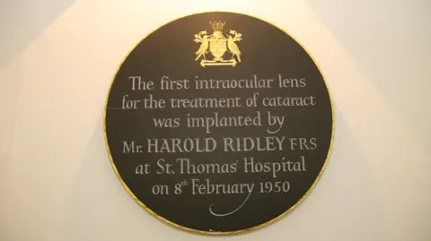 Guy’s and St Thomas’ NHS Foundation Trust An etched grey plaque with a gold border sits on a wall in Guy's & St Thomas' Hospital, reading: " The first intraocular lens for the treatment of cataract was implanted by Mr Harold Ridley at St Thomas' Hospital on 8 February 1950'