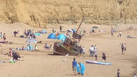West Bay Discovery Centre The boat sits tilted on the busy beach with the cliffs rising up in the background