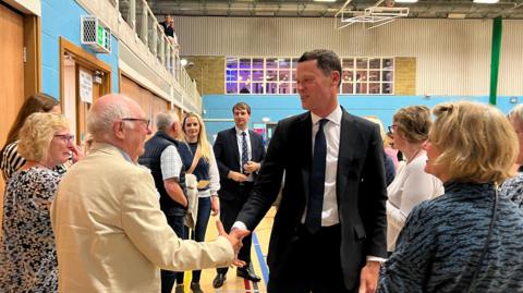 Alex Chalk shaking hands with someone at the count in Cheltenham at a leisure centre