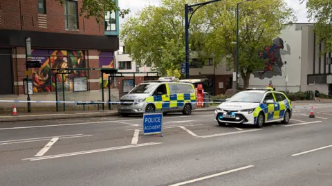 BBC Two police cars block a road with an accident sign and cordon tape surrounding them