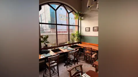 Richard Evans The inside of a coffee shop. The window is broken, and there is broken glass all over the floor of the coffee shop. There is a chair which appears to have been overturned.