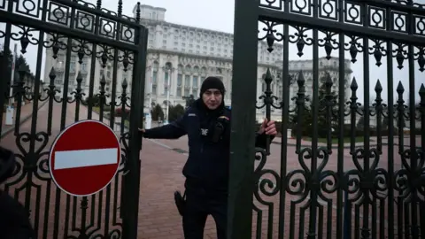 Reuters A police officer, wearing a dark hood and jacket, closes a wrought iron gate bearing a no entry sign at the grand Palace of Parliament