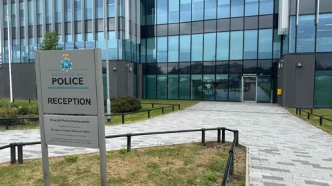 An outside view of a large glass fronted office building, with a sign showing the Merseyside Police crest. 