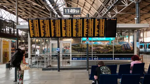 Getty Images A large arrival and departure board displays train schedules and destinations in a train station.