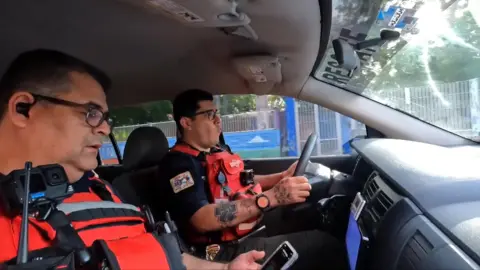 The two paramedics both wearing red stab vests and cameras, in their ambulance, on their way to an incident