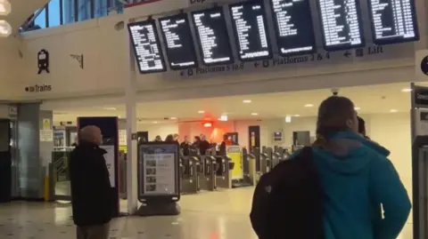 Two people look at train arrivals notices in a train station.