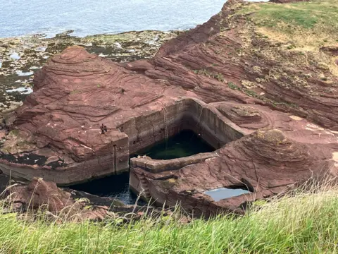 Raymond Hall Red rock with a small square cut out of it in the middle. There is a very small entrance.