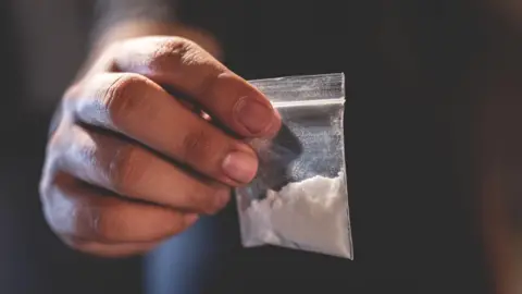 A bag of white powder is held in a man's hand.