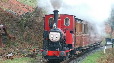 A red train is seen climbing through the woods on the approach to Nant Gwernol with a Tywyn - Nant Gwernol service. April 2004