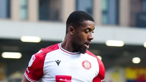 Jovan Malcolm with his head turned to the left and looking down towards where the ball is 