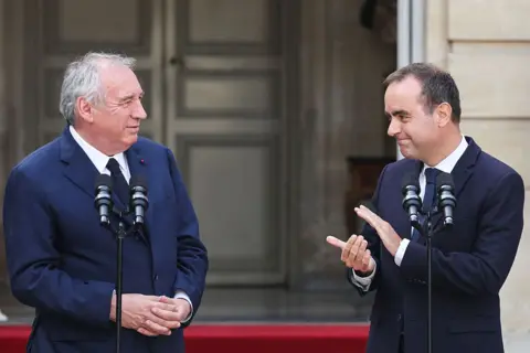 Getty Images Two men wearing blue suits stand next to one another behind microphones