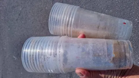 Weymouth and Portland Marine Litter Project Two stacks of dirty, clear, plastic, disposable cups in the palm of someone's hand.