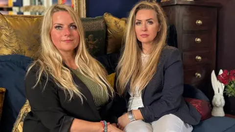 Pat's daughters Ashleigh Joachim and Lesley Haswell sitting side by side on a blue settee