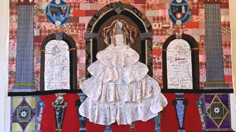 A colourful embroided woman, placed on a large sheet of fabric inside Hardwick Hall in Derbyshire.