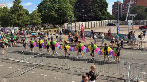 Jane Tomlinson's Run For All Picture of ten runners in a line ready to start the Ramathon, each joined by a multi-coloured tube creating a caterpillar costume. 
