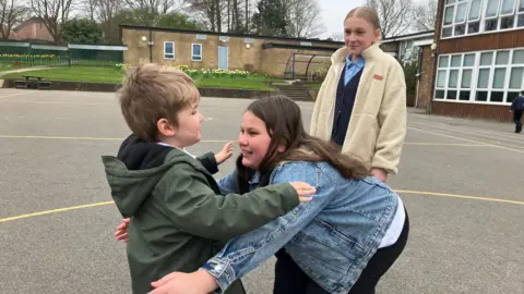 Children hug in a playground at Field Lane Primary School in Rastrick.