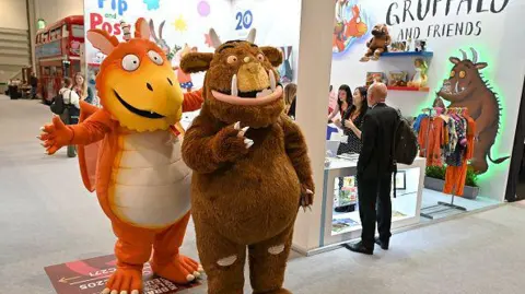 Getty Images The Zog and Gruffalo characters pose at an event in London in 2023. Zog is orange and white with a tail and Gruffalo is brown with horns, teeth and claws.