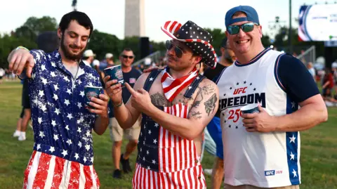 Three men pose for the camera - the two on the left are dressed in stars and stripes, while the man on the right smiles in a UFC Freedom 250 T-shirt