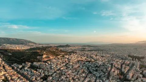 Stock aerial panoramic photo of Athens from the north at sunset, dusk - Psychiko, Chalandri, Marousi, Galatsi, nearby hills and the abandoned quarry of Psychiko up to the seaside