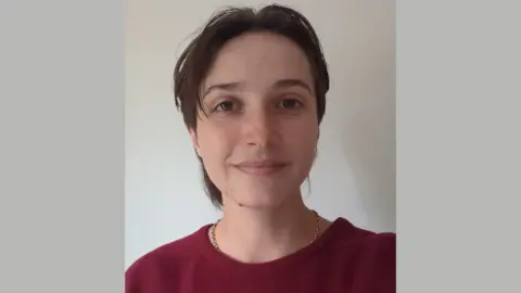 Contributed Freya stands facing the camera. She has short dark hair and is wearing a dark red jumper and a gold-coloured necklace