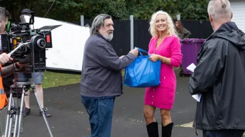Laima attēli Rikijs Tomlinsons ir attēlots komplektā ar Suzanne Collins uz dzīvojamo ielu, kas pazīstams kā Brookside Close. Viņš valkā džinsus un pelēku jaku, un viņa valkā rozā kleitu.