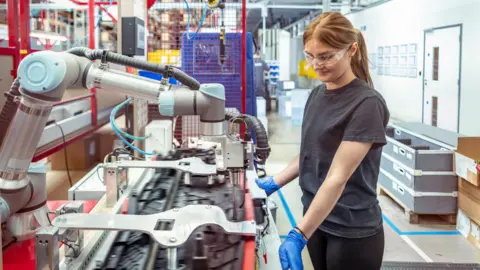 Getty Images Woman wearing rubber gloves and goggles looking down at manufacturing equipment