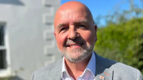 Deputy Jonathan Le Tocq, a bald man with a grey salt and pepper beard wearing grey suit.