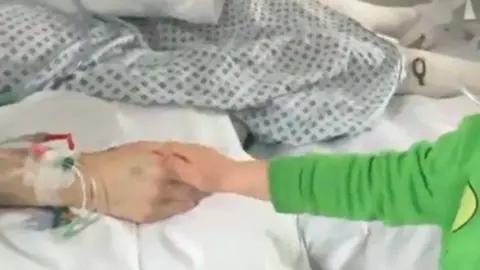 Family handout A child's hand seeing holding his mother's hand, who is in a hospital bed.