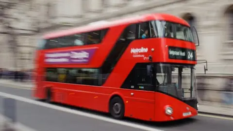 A red London bus driving down a street with a slight blur affect.