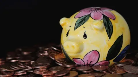 A yellow, pink and green piggy bank sitting on a pile of copper coins