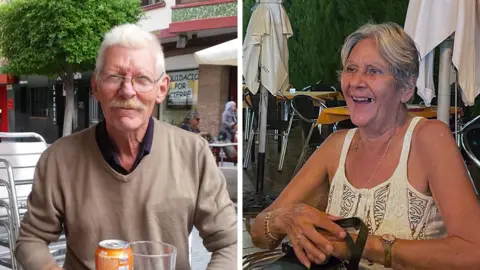 Family Terri (right) is wearing a white vest top and smiling with a bag on her lap. She has short, grey hair, or her hair is possibly tied back. Don is wearing glasses and has a moustache and is wearing a light brown jumper