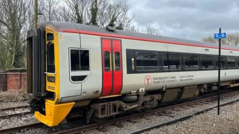 The side of a grey and red Transport for Wales train which is stopped on the racks at Shrewsbury Railway Station.