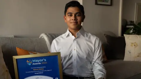 Rohan in his Kensington home holding two awards