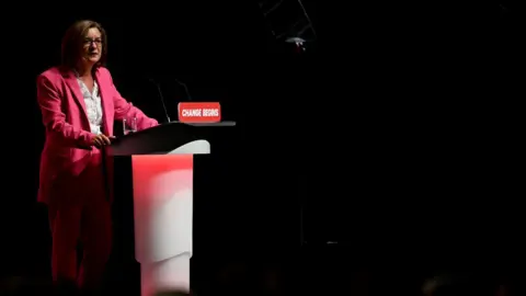 Getty Images Wales' First Minister Eluned Morgan stood behind a lectern. On it is a sign that says change begins. She is wearing a pink suit with a white shirt.