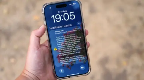 A mobile phone with a text message warning for the government which said there is a "very high risk of wildfires! and asked people not start a fire by setting off fireworks or lighting barbecues, fire pits or incinerators at home.