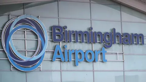 Reuters A sign saying "Birmingham Airport" in dark and light blue, on the side of a glass wall.