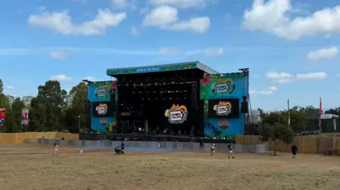 BBC An empty stage at Kendal Calling, with the festival branding. There are a handful of people in the field in front of the stage milling around.