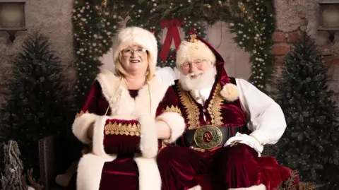 Danielle Axworthy Sharon and Allan Evans dressed as Santa and Mrs Claus, sat together with festive garlands in the background
